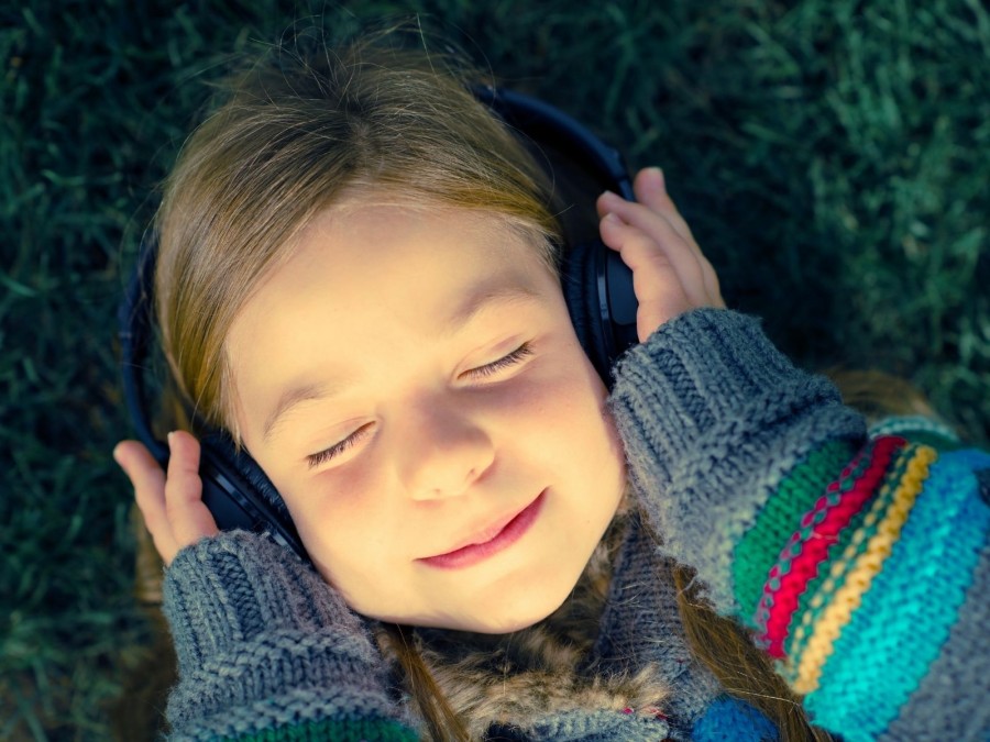 Kleines Mädchen mit Kopfhörern hört Musik zur Entspannung. Tagespflegenest, Kita, Kindergarten, Kinderbetreuung, Pflegevater, Pflegemutter - Canva