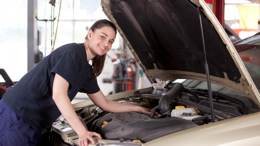 KFZ-Mechanikerin lächelnd an einer geöffneten Motorhaube eines Autos. Traumjob, Berufe, Praktikum, Praktika, Ausbildungsplatz - Canva