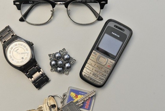 Ausschnitt aus dem Foto zu Fundsachen, Fundbüro: Das Bild zeigt eine Brille mit schwarzer Fassung, ein Handy, eine Brosche und den Teil eines Schlüsselbundes. - Walter Schernstein