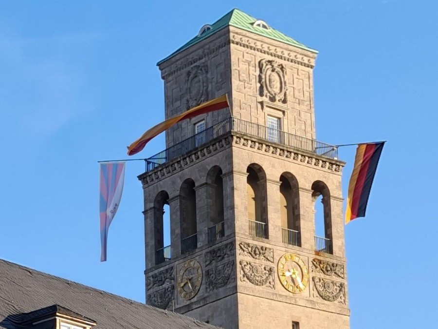 Rathausturm mit Beflaggung, auch die tibetische Flagge weht im Wind. Flagge zeigen für Tibet ist eine Kampagne der Tibet Initiative Deutschland e. V.. Seit 1996 Jahren rufen Städte, Gemeinden und Landkreise dazu auf, an dem Jahrestag des tibetischen Volksaufstands vom 10. März 1959, an ihren Rathäusern die tibetische Flagge zu hissen. - Jasmin Kramer
