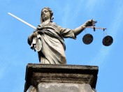 Justicia-Statue mit Waage und Schwert in den Händen, im Hintergrund blauer Himmel. Gerechtigkeit, Rechtsgrundlagen,  gesetzlichen Grundlagen 
