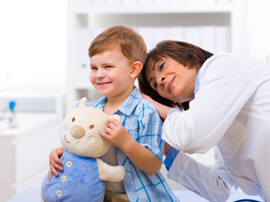 Ärztin untersucht einen kleinen Jungen mit einem Teddy auf dem Arm in der Kinderarztpraxis - Gesundheitsamt - Canva von StockLite