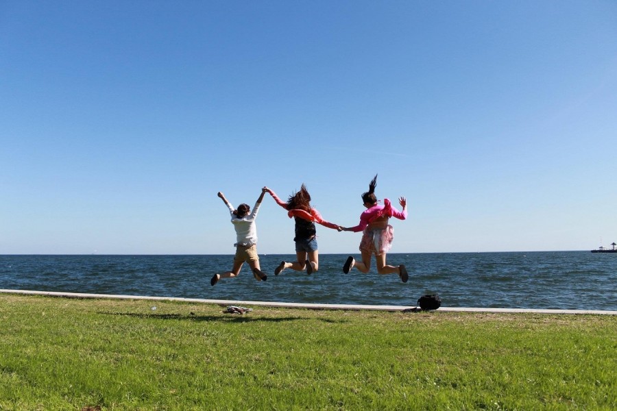 Drei Mädchen am Meer halten sich an den Händen und springen vor Freude in die Luft. Symbol für Schulferien, Urlaub - Bild von vuvuong auf Pixabay