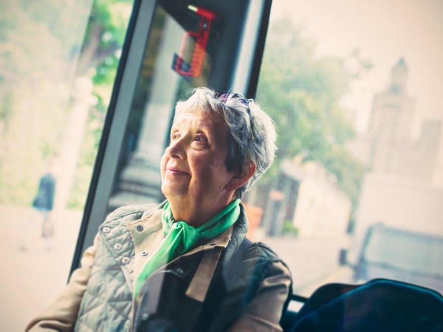 Seniorin sitzt imBus und schaut lächeln aus dem Fenster. Seniorinnenkulturbus, Seniorenkulturbus - Canva