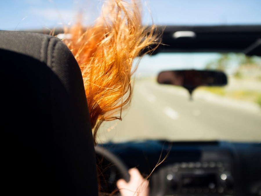 Bildausschnitt zeigt eine fahrende Person im Cabrio, die Haare wehen im Wind. Fahren in der Sommersaison. Infos zur Zuteilung eines Saisonkennzeichens. - Canva